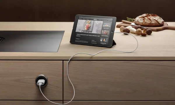 Tablet mit Rezept auf Küchenarbeitsplatte, daneben Brot, Pilze und modernes Kochfeld.