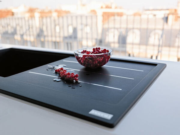 Eine Glasschale mit roten Johannisbeeren steht auf moderner schwarzer Küchenspüle.