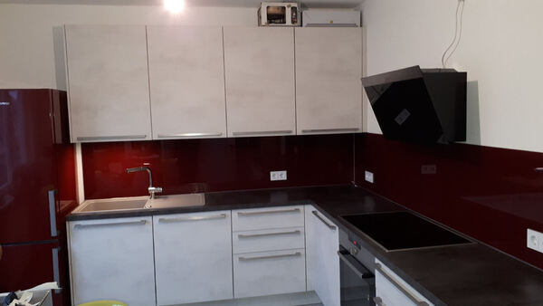 Moderne Einbauküche mit roten Glasrückwänden, weißen Schränken und schwarzen Elektrogeräten.