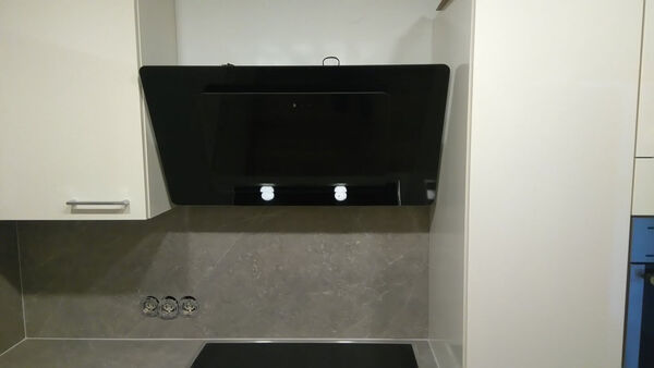 Moderne Dunstabzugshaube aus Glas in weißer Einbauküche mit grauer Küchenrückwand.