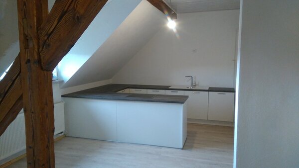 Moderne Einbauküche mit Dachschräge, Holzoptik-Arbeitsplatte und offenem Wohnbereich.