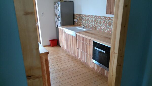 Moderne Küche mit Holzfronten, buntem Fliesenspiegel und Einbaugeräten auf Holzboden.