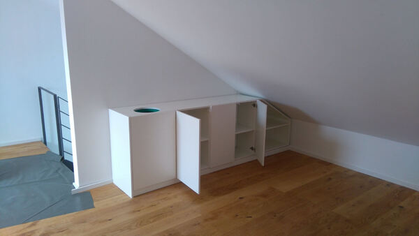 Weißes Einbauregal mit offenen Türen unter Dachschräge auf Parkettboden in modernem Raum.
