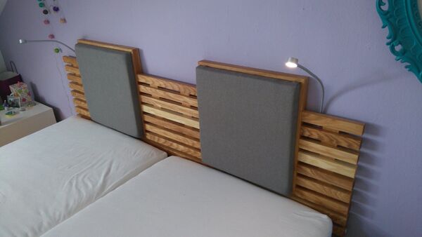 Modernes Doppelbett mit Holz-Kopfteil, grauen Polsterlehnen und LED-Leseleuchten.