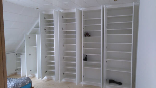 Weiße Einbauschränke mit vielen Regalen unter einer Dachschräge im Schlafzimmer.