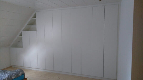 Ein weißer, maßgefertigter Einbauschrank passt sich einer Dachschräge im Schlafzimmer an.